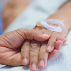 Dłoń trzymająca dłoń, z wenflonem. Symboliczne ujęcie końca życia, nieuchronnej śmierci ze starości.