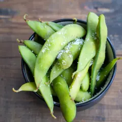 Grüne Edamame-Schoten, leicht gesalzen, in einer Schüssel auf Holzhintergrund. Was sind Edamame? Ein gesunder Snack!