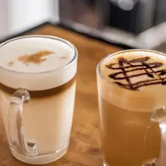 Dwie pyszne kawy latte, jedna z czekoladowym wzorem, druga z pianką i cynamonem. Idealne na chwilę relaksu.