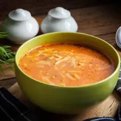 A miseczka zielona z najlepszą zupą pomidorową przepis babci, z makaronem i przyprawami. Obok łyżka i serwetka.