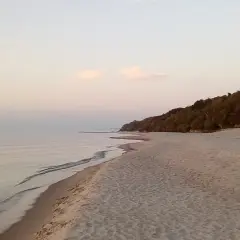 Spokojna plaża z piaszczystym brzegiem i lasem na wzgórzu. Idealne miejsce dla małych miejscowości nad morzem.
