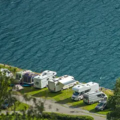 Un garaje al aire libre con varias caravanas y autocaravanas aparcadas junto a un lago azul.