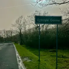 Znak drogowy z napisem "Ustrzyki Górne" na tle mokrej drogi i drzew.