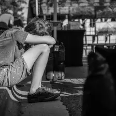 Chłopiec skulony na chodniku, zamyślony. Leczenie psychiatryczne a opieka nad dzieckiem to trudne wyzwania dla rodziny.