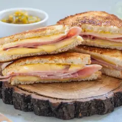Pile de croque monsieur dorés, garniture généreuse de jambon et fromage fondant, servis sur une tranche de bois rustique.