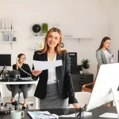 Kobiety w biurze, jedna trzyma dokumenty, druga rozmawia przez telefon.
