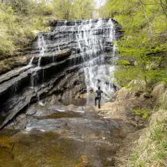 Cascada en un bosque frondoso, ideal para descubrir la **que ver en Burgos naturaleza**. Un hombre contempla la fuerza del agua.