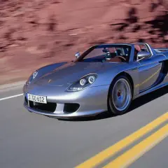 Srebrny Porsche Carrera GT pędzi po pustynnej drodze, zostawiając za sobą rozmyte czerwone skały.