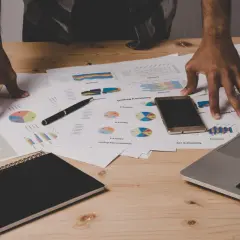 Ręce nad dokumentami z wykresami i raportami, laptop, telefon i notatnik. Analiza danych i data warehouse design.