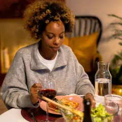 Mujer con cabello rizado mira su plato de comida, pero no come porque no tengo hambre. Hay vino y ensalada en la mesa.