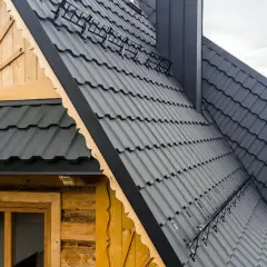 Nowoczesny dach mansardowy z grafitowej blachodachówki, przylegający do drewnianej ściany z oknem.