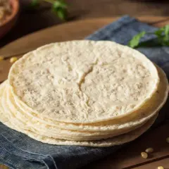 Stos świeżo upieczonych placków tortilla, które wyglądają jak z oryginalny przepis, leży na niebieskiej serwetce.