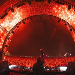 DJ z uniesioną pięścią na tle tłumu i fajerwerków. Niezapomniany sunrise lineup na festiwalu.