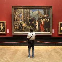 A person contemplates a large painting in a museum, perhaps inspired by the best art history graduate programs.