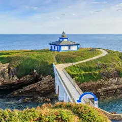 Faro y casa azul en una isla verde, conectada por un puente blanco sobre el mar Cantábrico en Lugo.