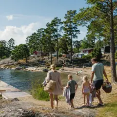 Familj på väg mot vattnet för en härlig semester med bebis i Sverige. Barnen springer glatt mot bryggan där andra badar.