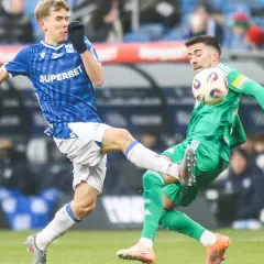 Dwóch piłkarzy walczy o piłkę. Jeden w niebieskiej koszulce, wychowanek Lecha Poznań, próbuje odebrać futbolówkę przeciwnikowi w zielonym stroju.