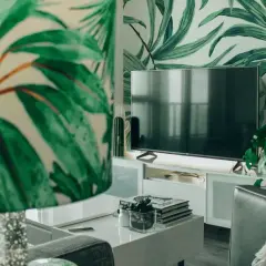 Sala de estar con papel tapiz de hojas tropicales. Muebles DM blancos y un televisor moderno.