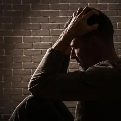 Uomo seduto con le mani tra i capelli, illuminato da un raggio di luce. Potrebbe cercare sollievo con stabilizzatori dell'umore naturali.