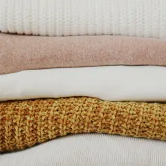 Stos ubrań: biały sweter, różowa bluza, biała koszulka, brązowy sweter.