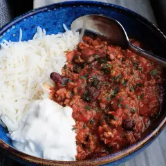 En blå skål med ris, en klick gräddfil och en portion av det godaste chili con carne, toppad med persilja.