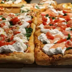 Pyszna pizza włoska na cienkim cieście z burratą, pomidorkami i łososiem.
