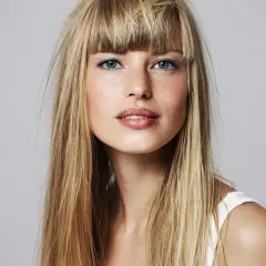 Blonde Frau mit blauen Augen und einem leichten Lächeln. Sie fragt sich, wie oft Haare blondieren für diesen Look nötig ist.