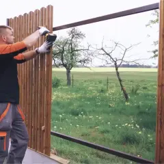 Pracownik dokonuje montażu sztachet drewnianych, przykręcając je do metalowej konstrukcji.