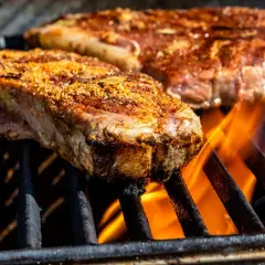 Deux entrecôtes au grill, assaisonnées et grillées à la perfection, avec des flammes vives en dessous.