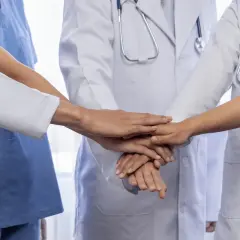 Lekarze w białych fartuchach i niebieskich uniformach łączą dłonie, symbolizując współpracę i siłę spółki partnerskiej.