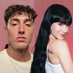 Plex y Aitana, dos jóvenes con miradas intensas, posan juntos en un estudio con fondo rosa.