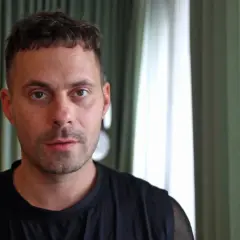 Oskar Linnros i en intervju, med gröna gardiner i bakgrunden.