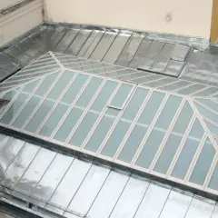 Dachdecker arbeitet an Glasdach-Fugen abdichten. Metallbedecktes Dach mit Glasflächen und einem kleinen Lüftungsfenster.