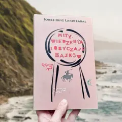 Książka "Mity, wierzenia i obyczaje Basków" Jorge Ruiza Lardizabala, z ilustracjami przedstawiającymi rycerza na koniu i inne symbole, na tle malowniczego wybrzeża.