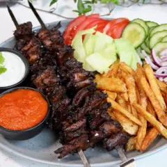 En tallrik med vegetarisk kebab på spett, serverad med pommes frites, sallad, tomat, gurka, rödlök, vit sås och en röd sås.