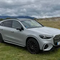 Un SUV gris moderno, con tracción 4 matic, descansa en un campo verde con montañas nubladas al fondo.