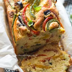Plumcake salato ricco di verdure colorate come zucchine, peperoni e olive, guarnito con basilico fresco.