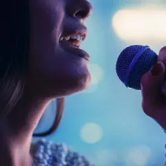Kobieta śpiewa do mikrofonu, jej głos rozbrzmiewa w rytm muzyki. To idealny moment na playback.