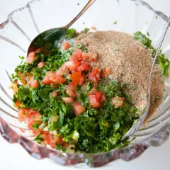 En skål med färsk persilja, tomat och finmalet vete för tabbouleh utan bulgur.