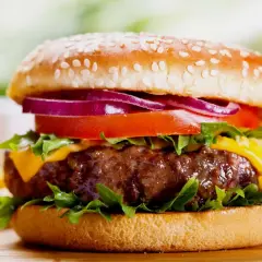 Soczysty burger z serem, pomidorem, czerwoną cebulą i sałatą na bułce z sezamem.