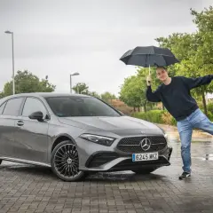 Hombre con paraguas posa junto a un Mercedes Clase A gris. ¡Una prueba de conducción bajo la lluvia!
