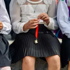 Dzieci w szkolnych strojach trzymają dzwoneczki na czerwonej wstążce. Czy to symbol końca roku i nadzieja na średnią na czerwony pasek w 4 klasie?