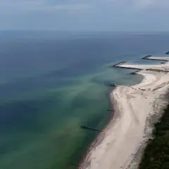 Plaża w Jarosławcu, zwana czasem "plażą dubaj", z kamiennymi falochronami i zielonym lasem.