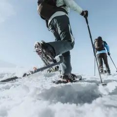 Deux personnes font une randonnée dans la neige, leurs raquettes s'enfonçant dans la poudreuse. Le ciel bleu clair promet une belle journée d'aventure.