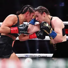 Two professional female boxers clash heads in the ring, their faces intense as they block punches.