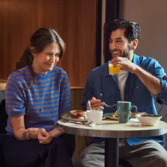 Ett leende par njuter av en god frukost på Scandic Örebro. Mannen dricker apelsinjuice medan kvinnan ler åt honom.