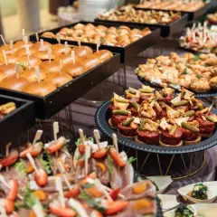 Stół z przekąskami: mini burgery, croissanty, tartinki, koreczki z owocami i mięsem.