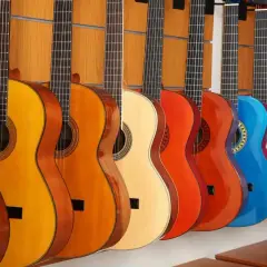 Rząd kolorowych gitar akustycznych, od pomarańczowej po czerwoną i niebieską, prezentuje różne rozmiary i odcienie.
