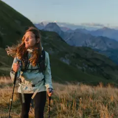 Kobieta z kijkami do **speed hikingu** podziwia alpejski krajobraz o zachodzie słońca.