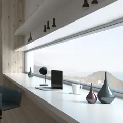 Szeroki parapet z widokiem na morze, na którym stoi laptop, lampka i ozdobne wazony. Obok krzesło.